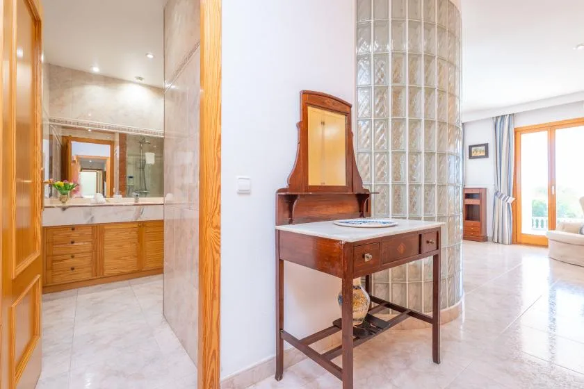 A bright interior shows a wooden console beside a glass-block partition and an open bathroom.