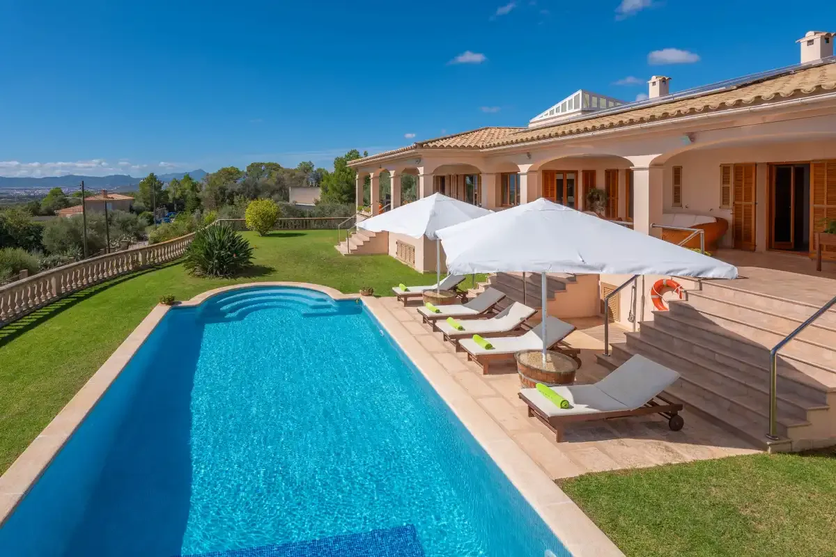 A swimming pool beside a terrace with shaded loungers and a lawn.