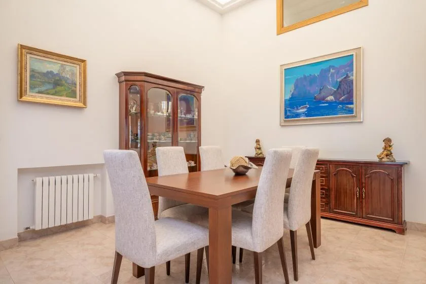 A dining room with a wooden table and upholstered seating beneath framed paintings.