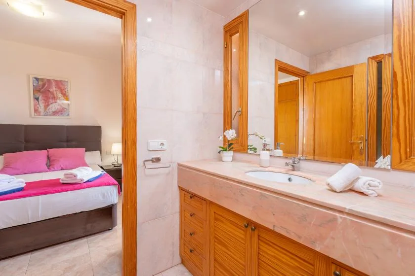 A tiled bathroom with a long vanity and a view into a bedroom.