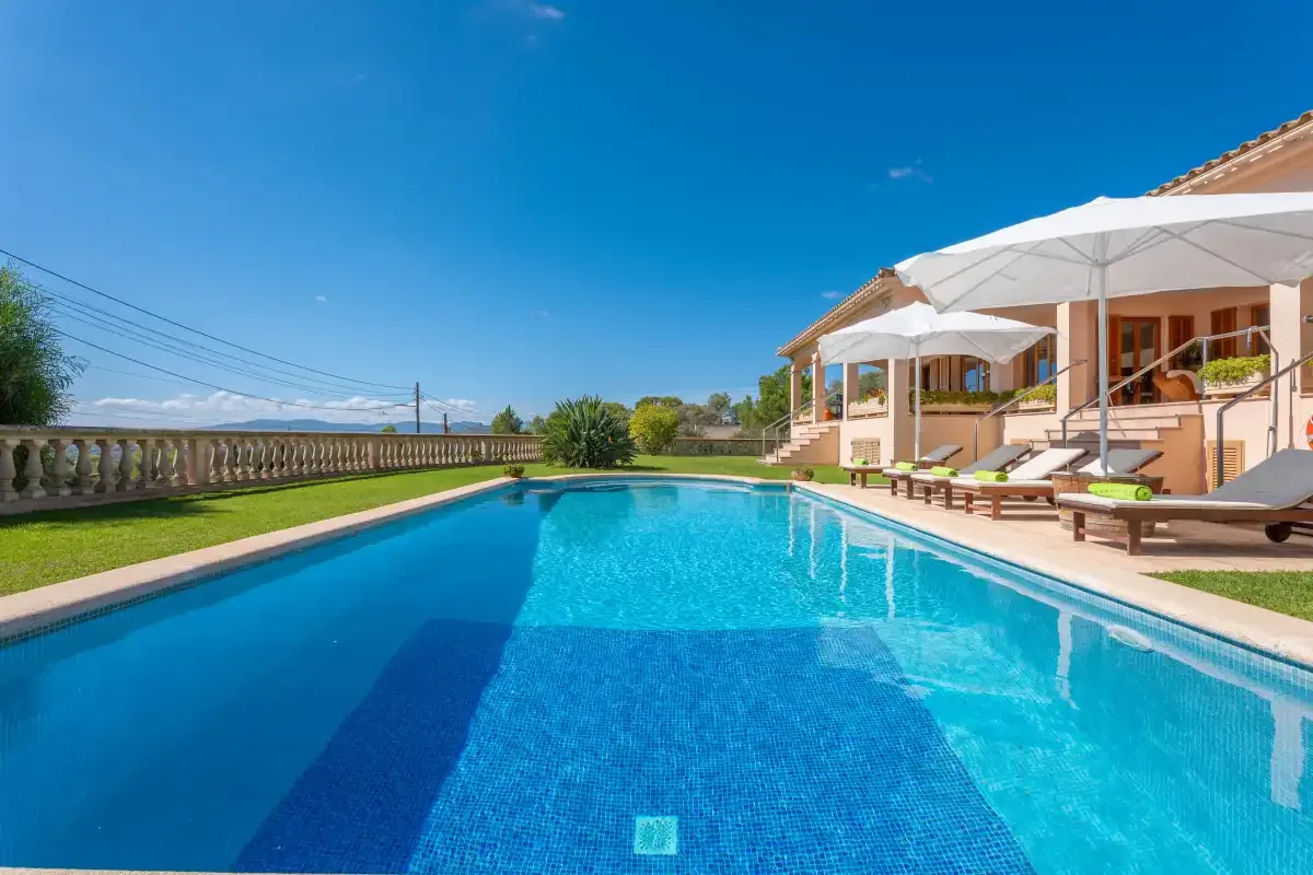 An outdoor swimming pool beside a patio with sun loungers and umbrellas.