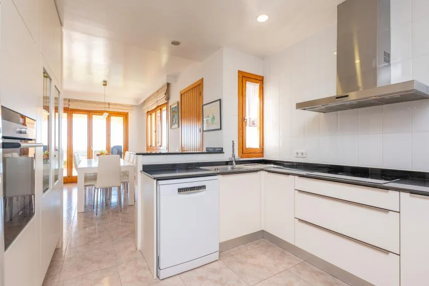 A bright kitchen with white cabinets and a dining area visible beyond.