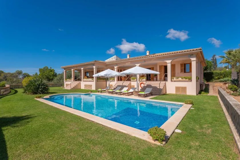 A house and swimming pool sit in a landscaped garden under a clear sky.