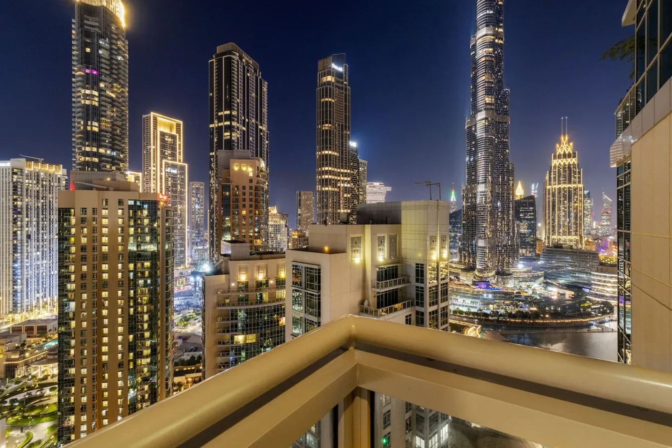 A nighttime city skyline viewed from a balcony, with illuminated high-rise buildings.