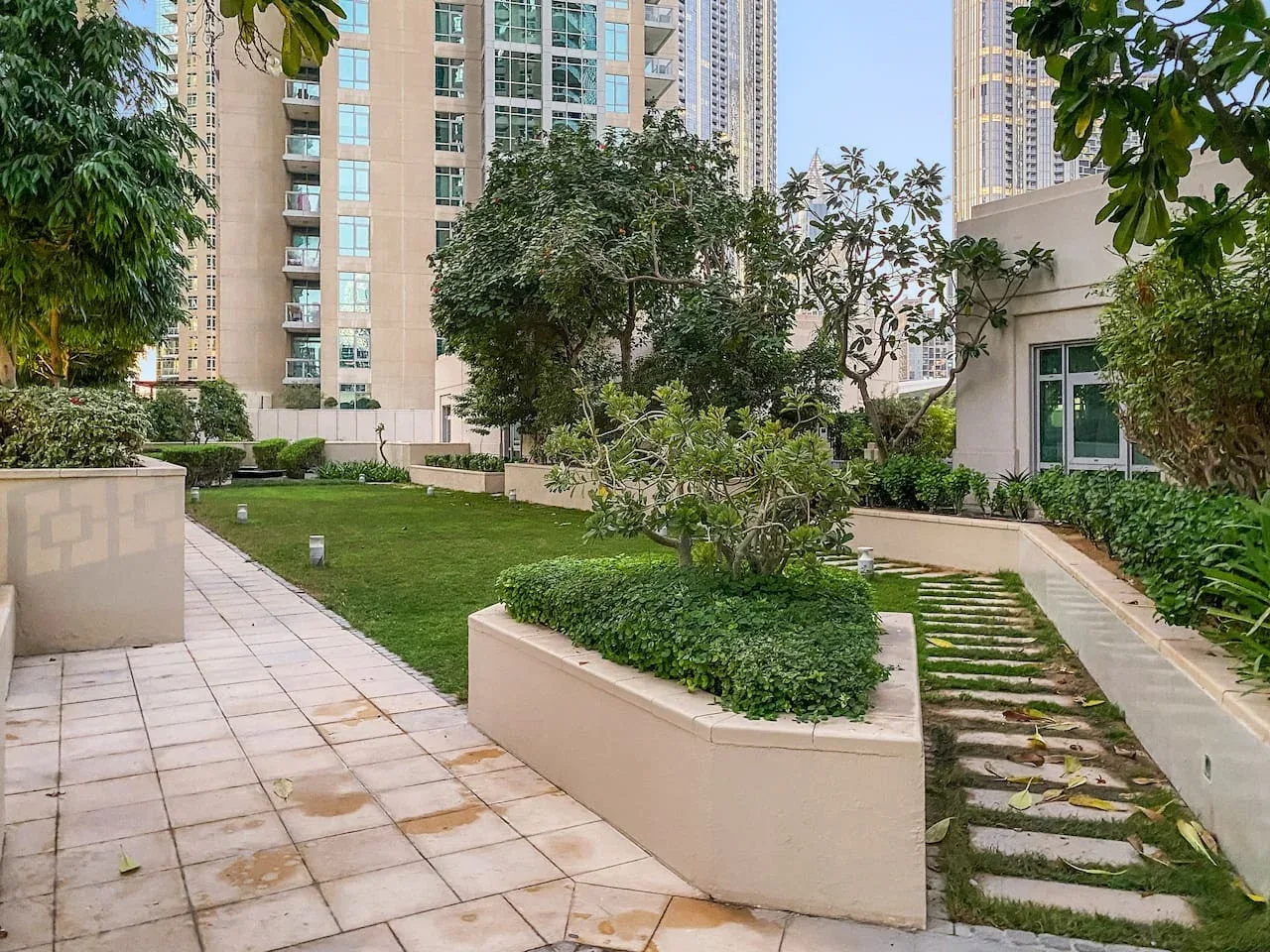 A landscaped courtyard with paved paths, planted beds, and surrounding high-rise buildings.
