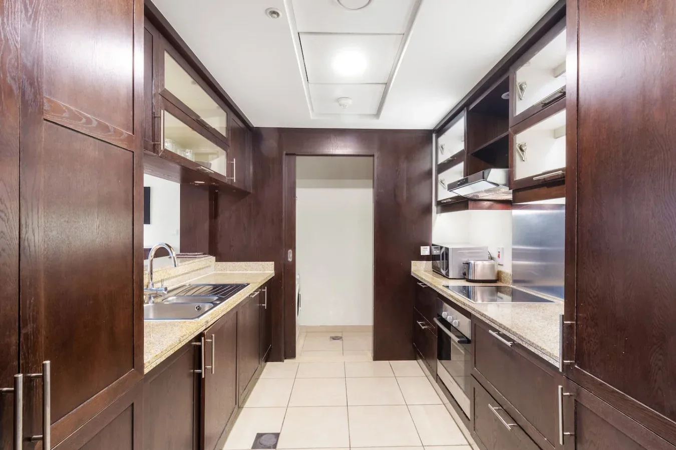 A narrow kitchen with dark cabinets, countertops, and built-in appliances.