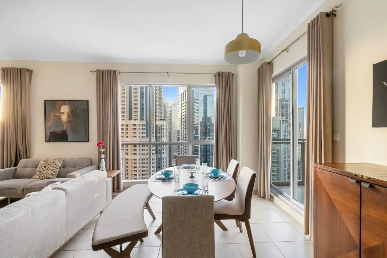 A living and dining area with seating, a table, and large windows overlooking nearby buildings.