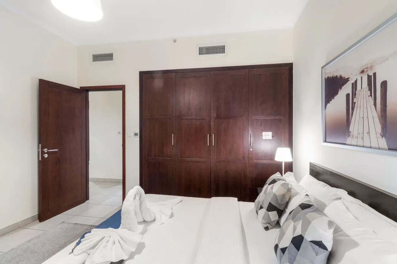 A bedroom with a large dark wooden wardrobe and a neatly made bed.