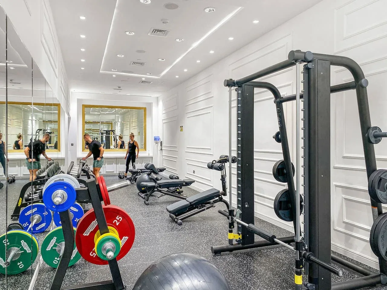 A gym with weightlifting equipment and mirrored walls.