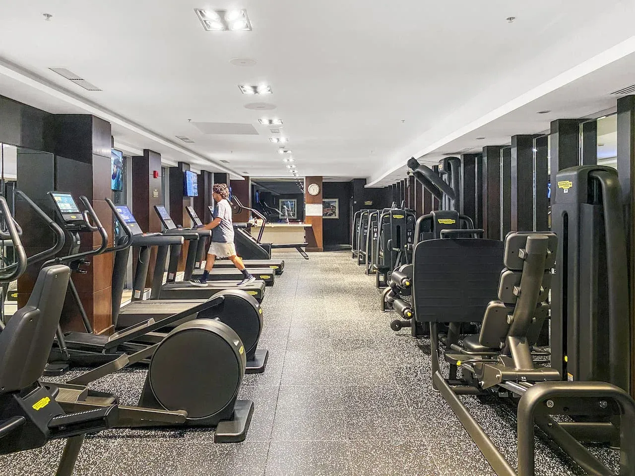 A fitness room with exercise machines arranged along both sides.