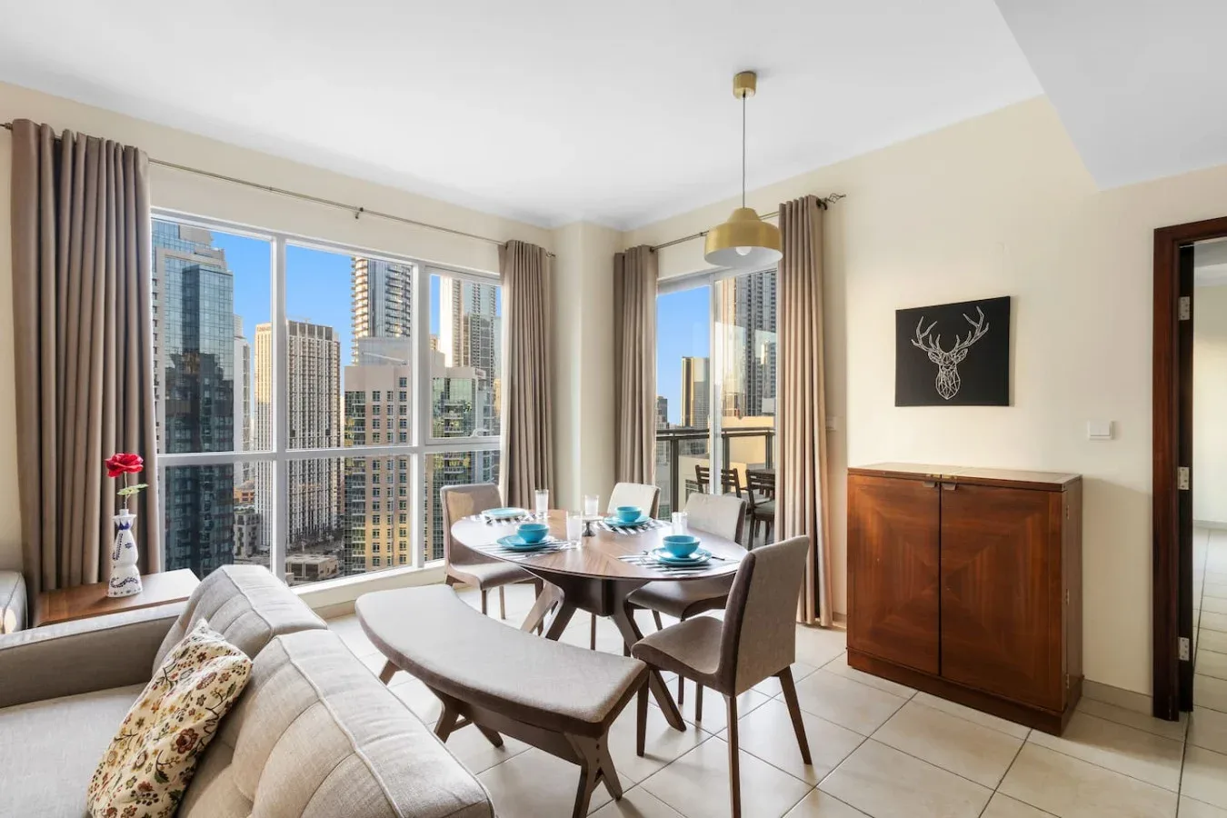 A bright dining and living area has large windows overlooking nearby city buildings.