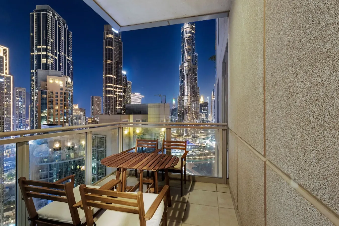 A balcony seating area overlooks illuminated city skyscrapers at night.
