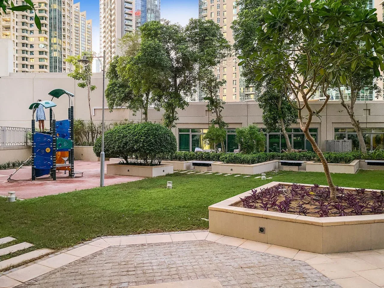 A landscaped courtyard with a small playground, trees, and apartment buildings.