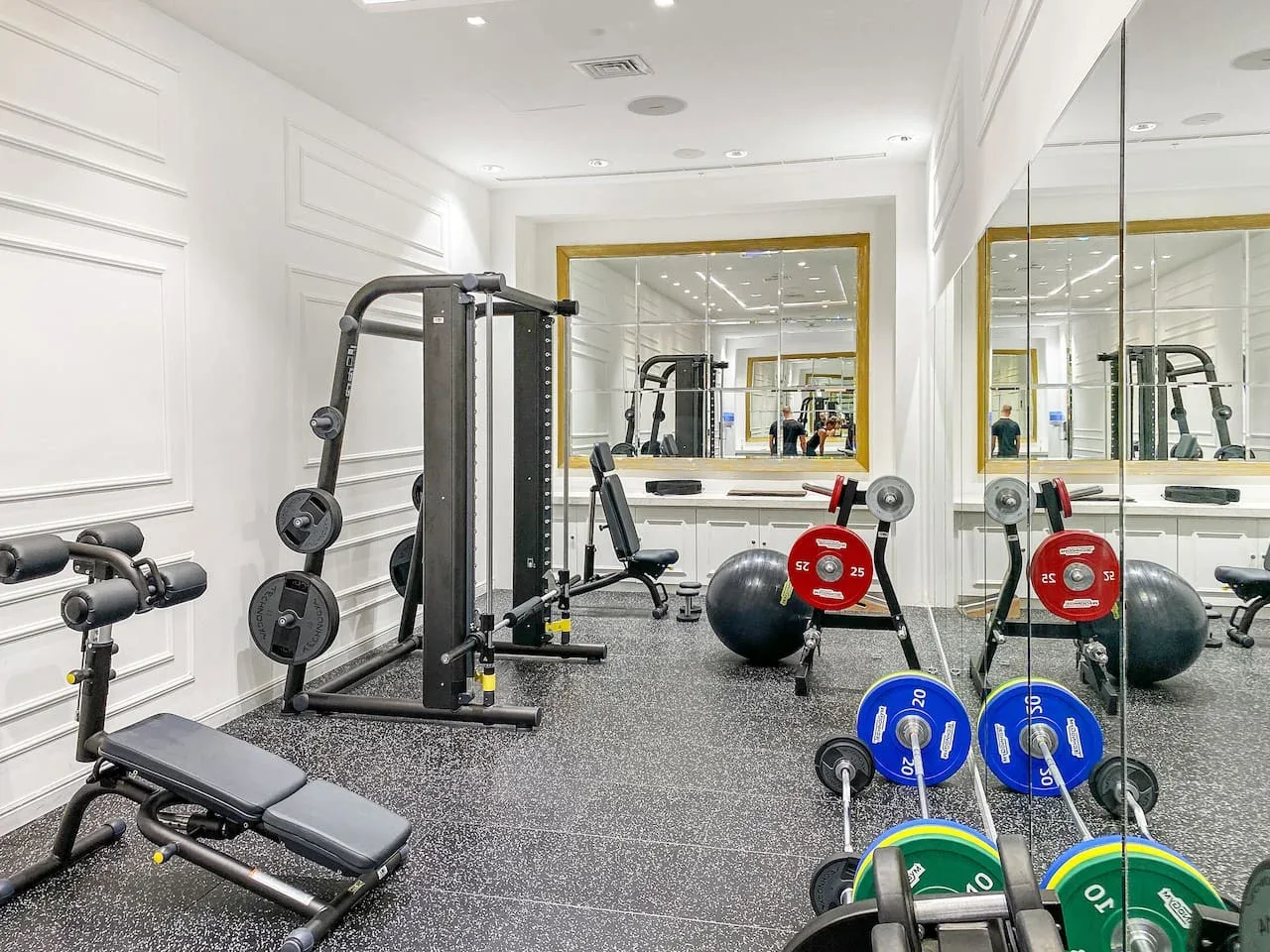 A home gym with weight machines and exercise equipment reflected in a wall mirror.
