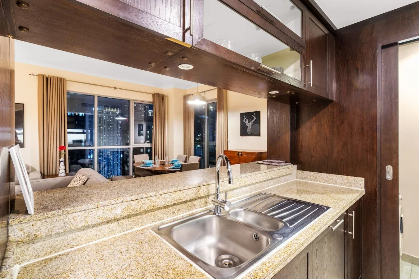 A kitchen counter with a double-basin sink overlooks a dining area and large windows.