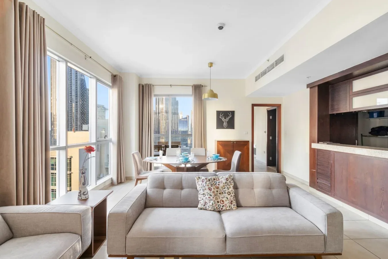 A bright living room with gray seating and floor-to-ceiling windows overlooking city buildings.
