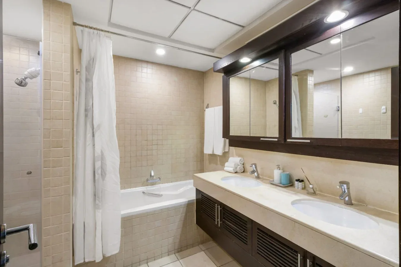 A tiled bathroom with a bathtub, shower curtain, and long sink counter.