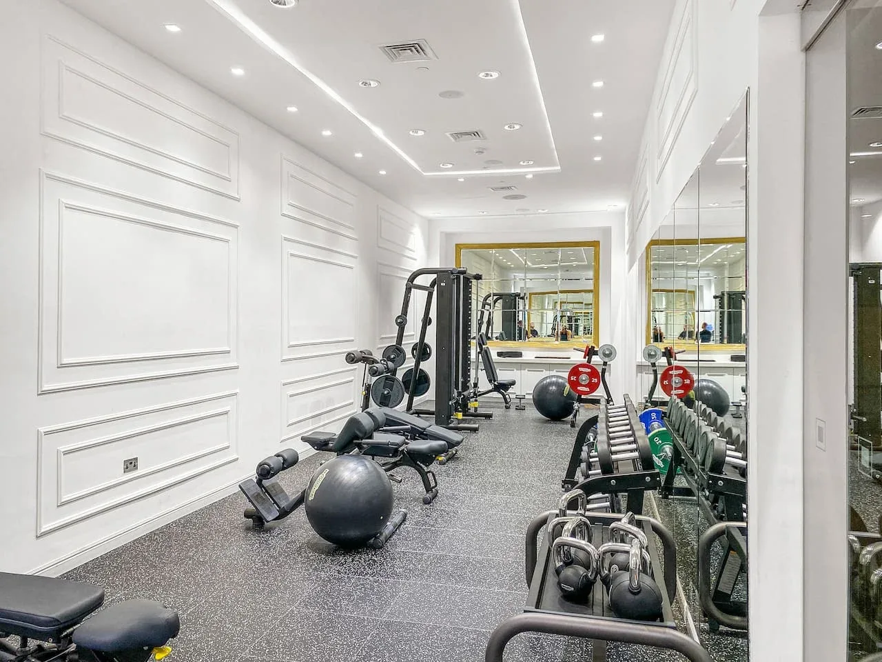A gym with exercise machines, weights, and mirrors along the walls.