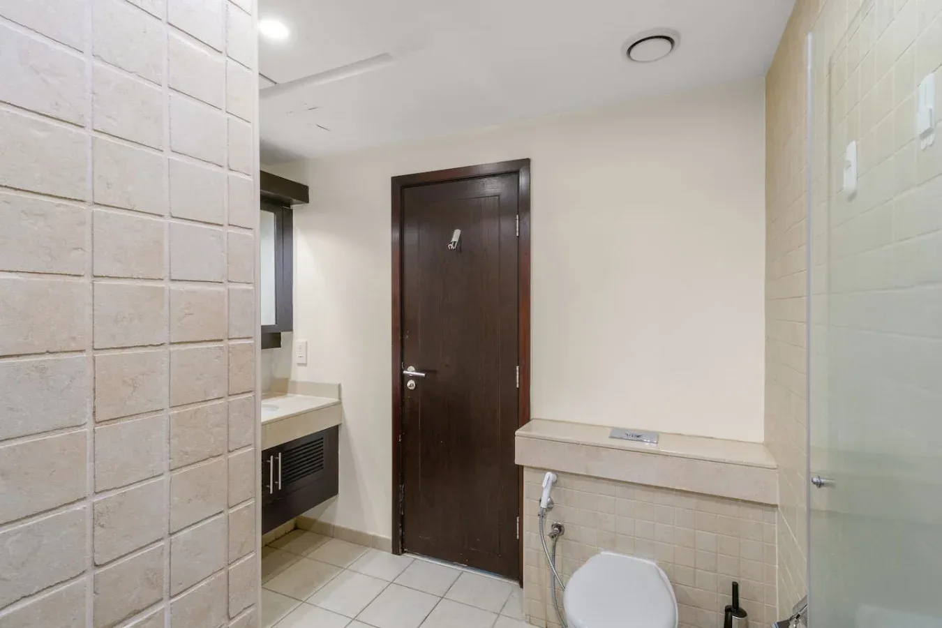 A tiled bathroom with a toilet, sink, and dark wooden door.