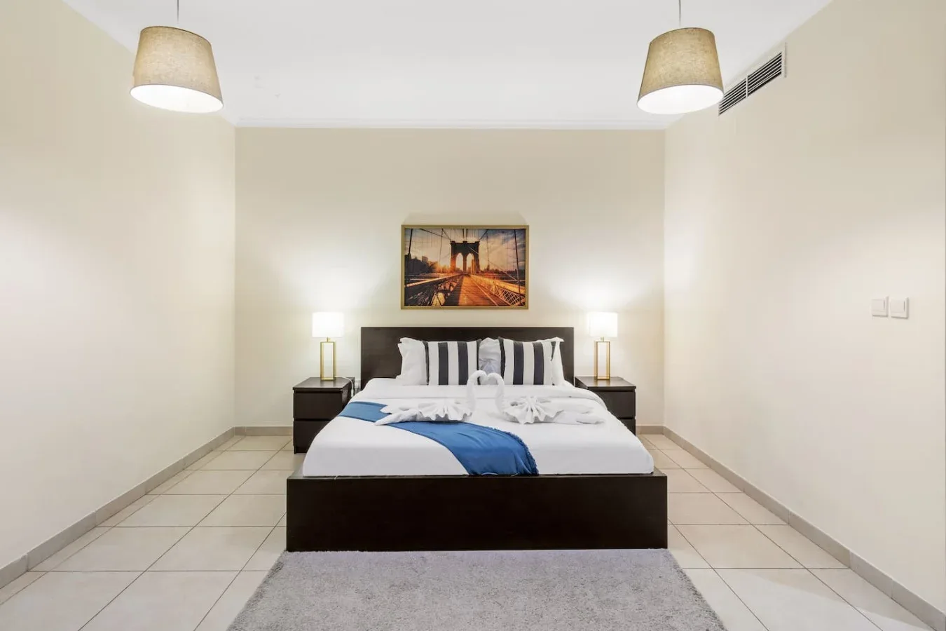 A bedroom with a neatly made bed, bedside lamps, and framed artwork.
