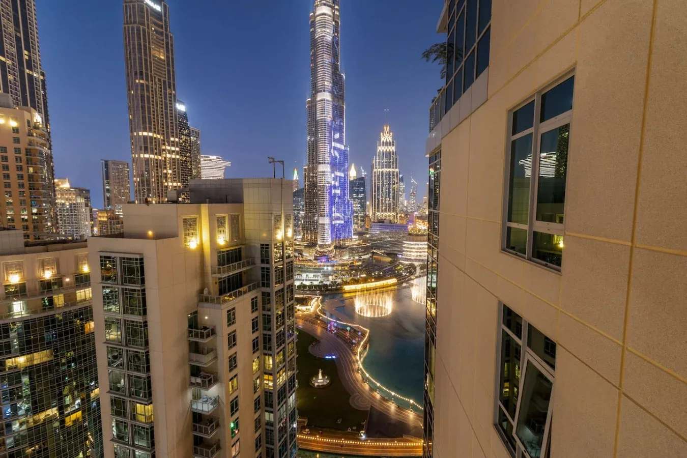 A nighttime city skyline overlooks illuminated towers and a waterfront.