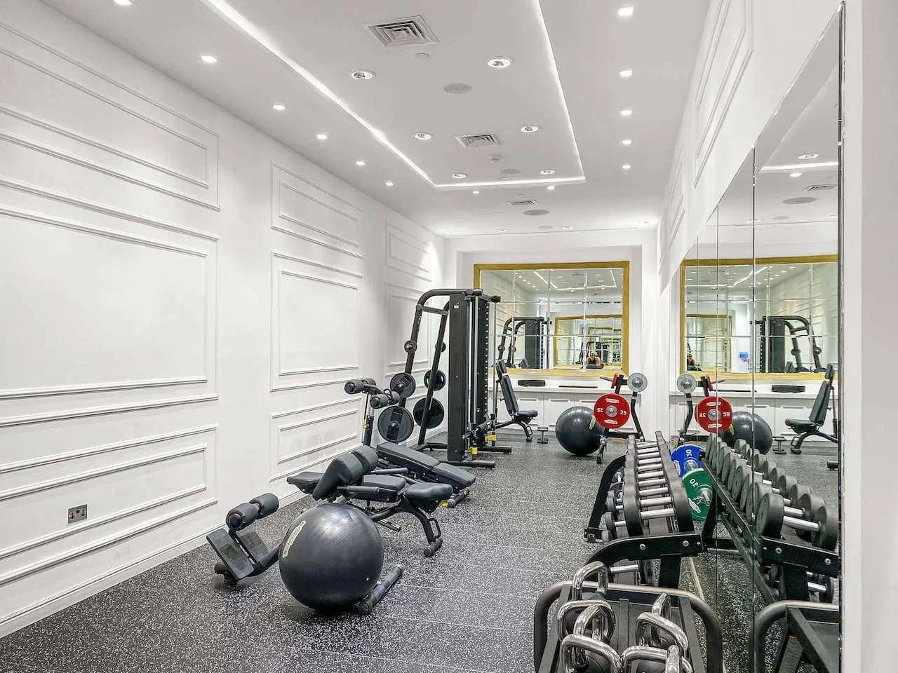 A gym with exercise equipment, free weights, and a mirrored wall.