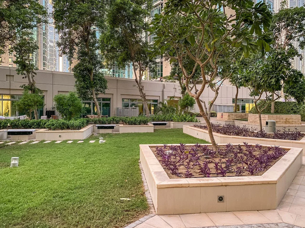 A landscaped courtyard with a lawn, planted beds, and trees beside a modern building.