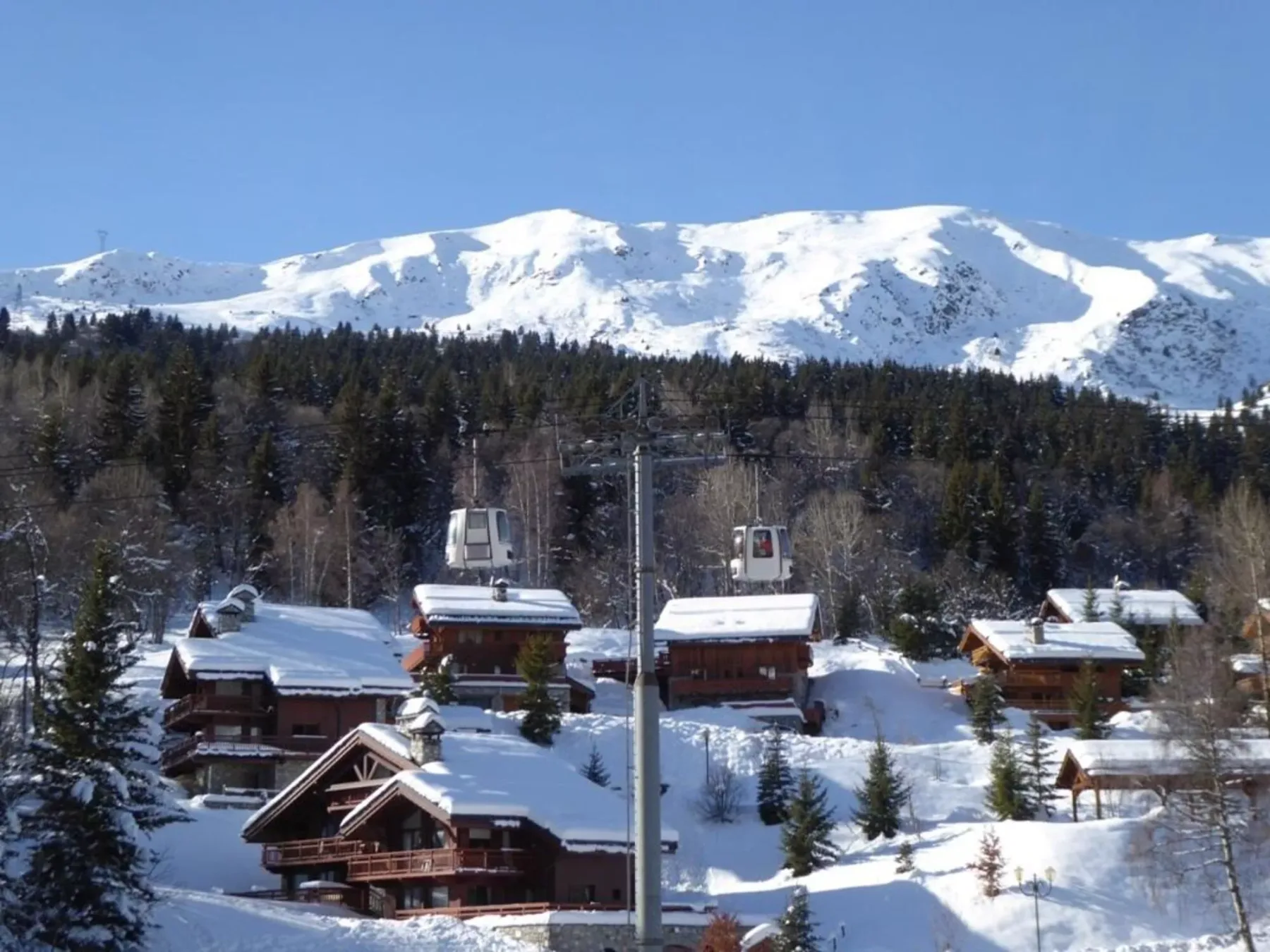 Cabañas cubiertas de nieve se encuentran bajo una ladera boscosa y una cordillera.