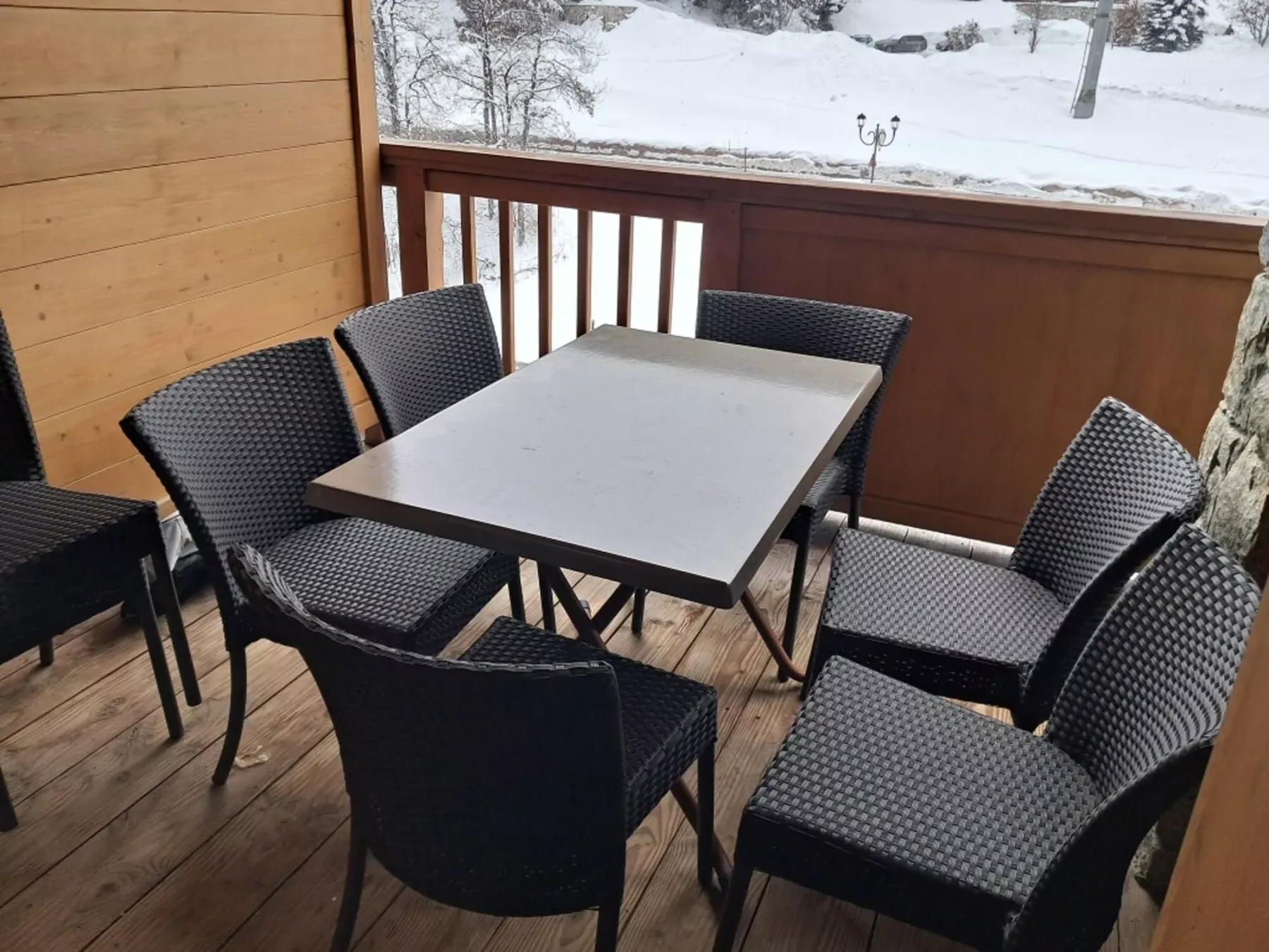 Un balcón amueblado con mesa y asientos da a un paisaje nevado.