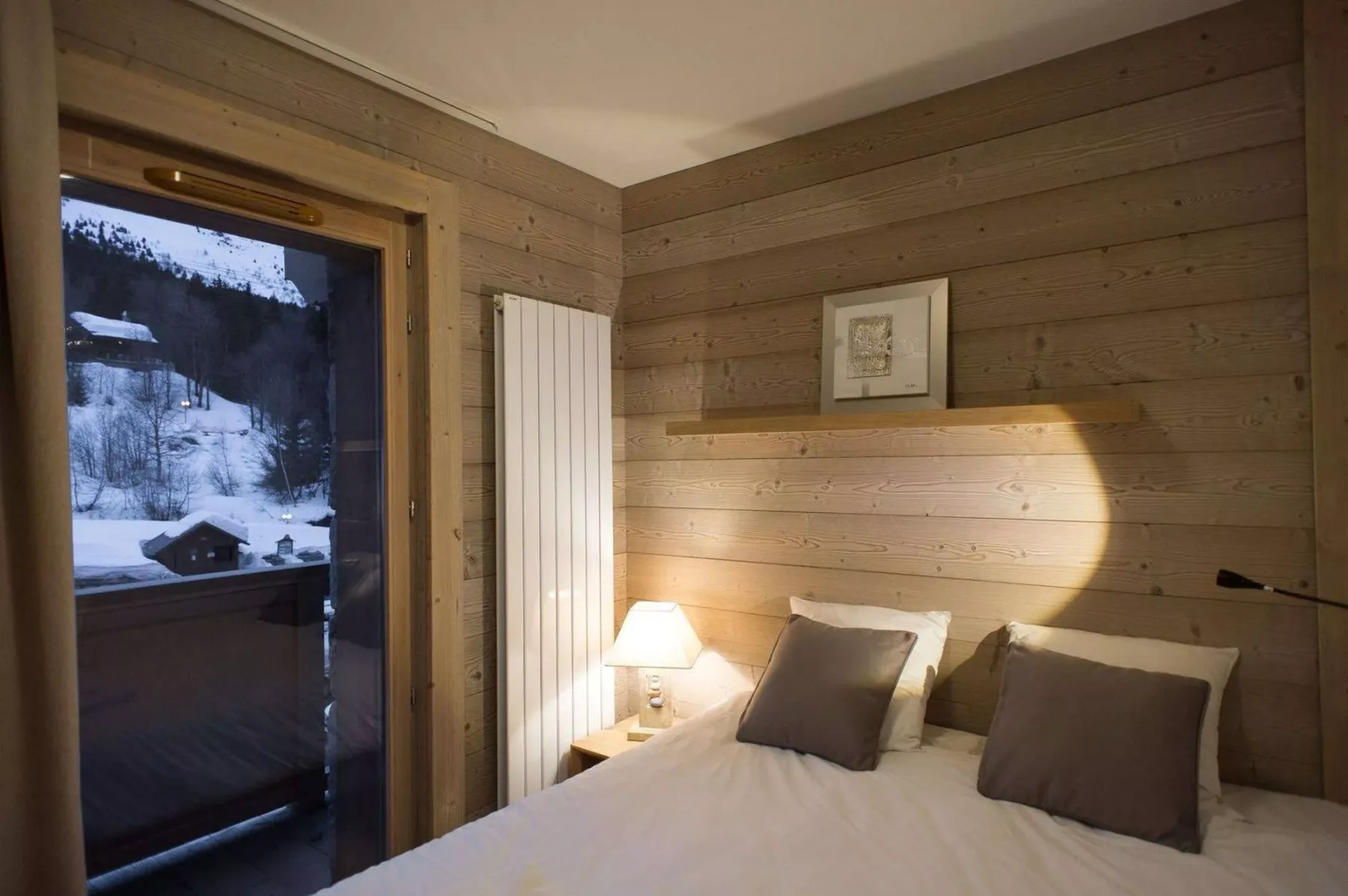 A bedroom with a bed beside a glass door overlooking a snowy landscape.
