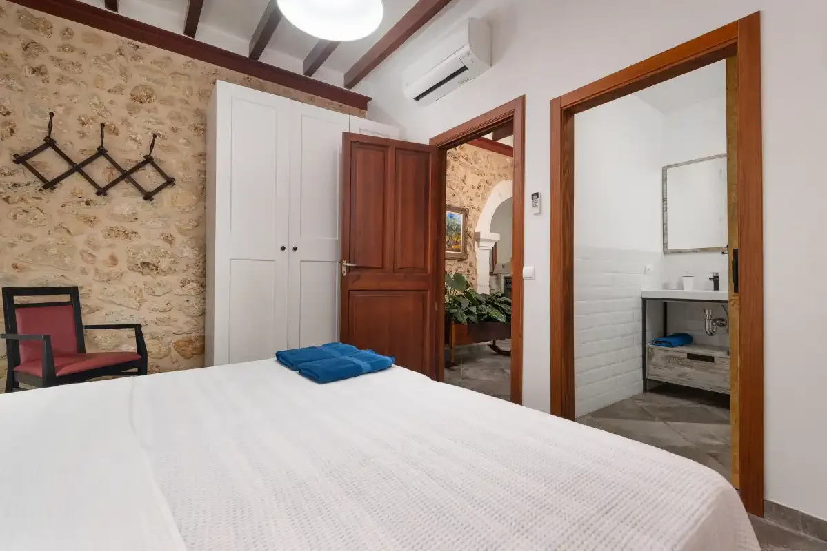 Un dormitorio con ropa de cama blanca, un armario y una puerta de madera abierta.