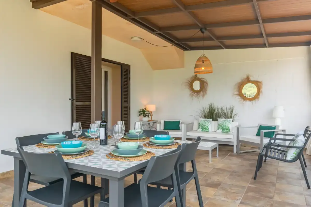 Una zona cubierta de comedor y descanso con una mesa puesta y muebles blancos.