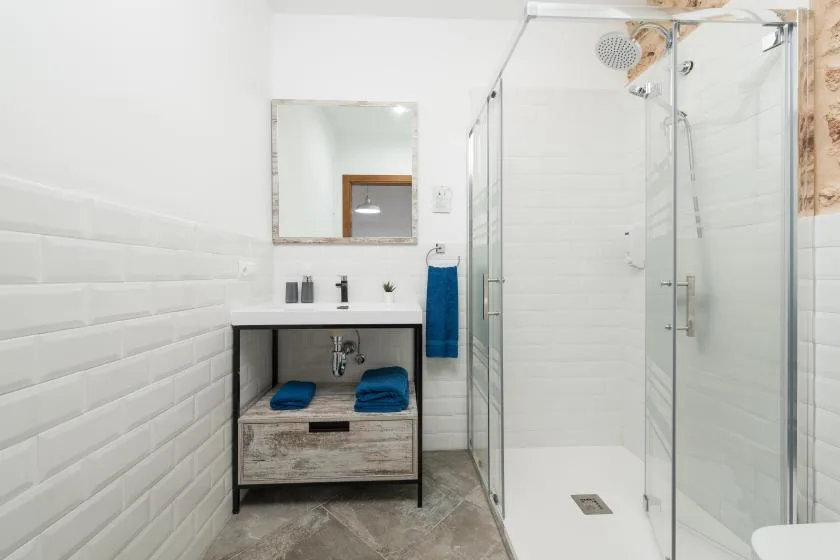 Un baño luminoso con una ducha de vidrio y un mueble de lavabo.