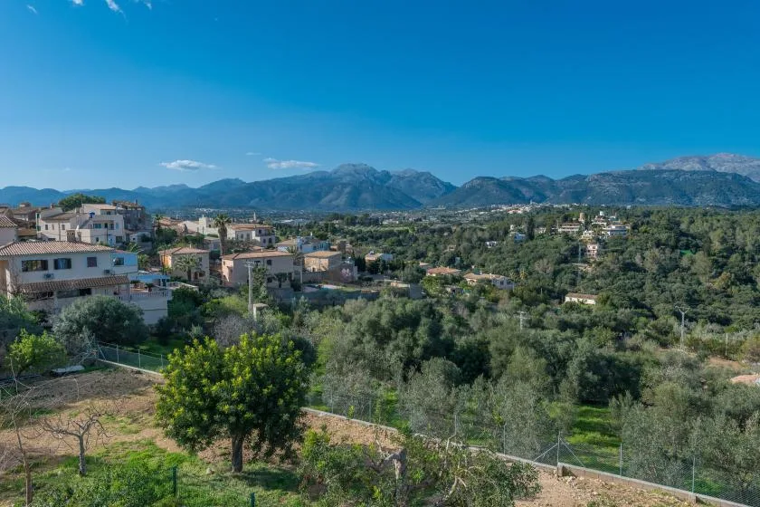 Un paisaje rural con casas dispersas, árboles y montañas a lo lejos.