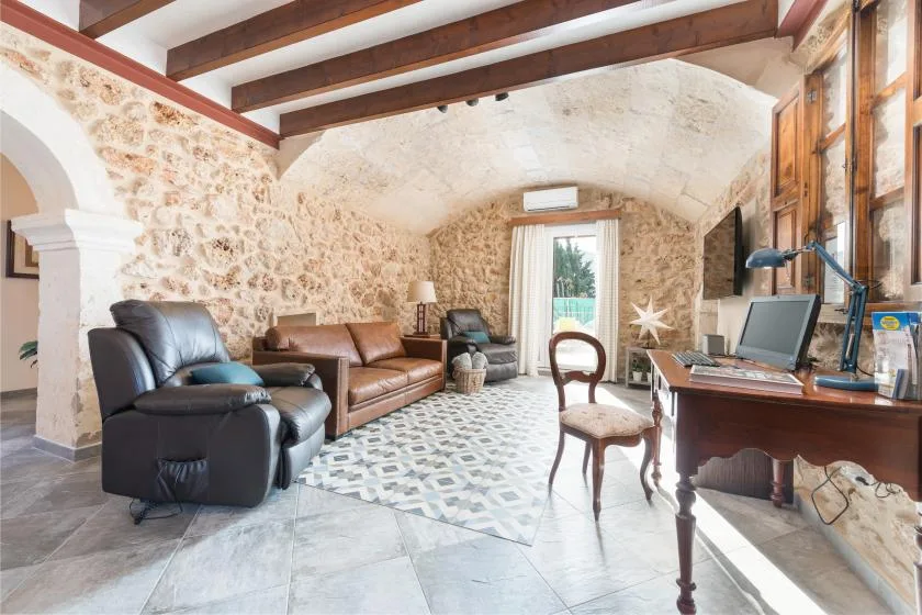 Una sala de estar con paredes de piedra, asientos, un escritorio y vigas expuestas.
