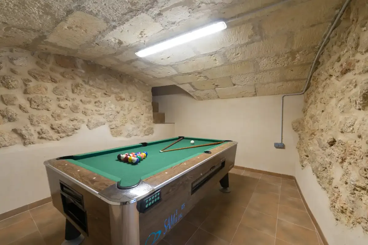 Una sala de billar con una mesa verde bajo un techo bajo de piedra.