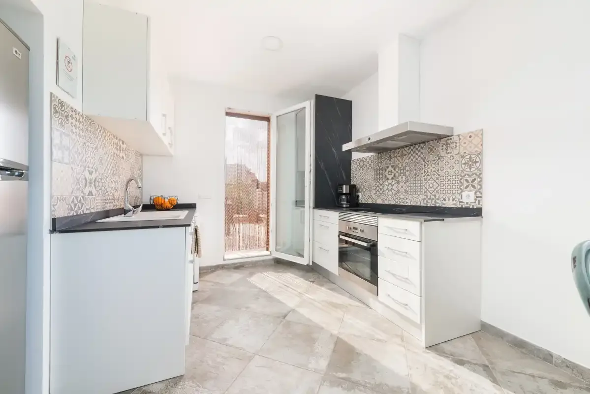 Una cocina luminosa con armarios blancos, salpicadero estampado y una puerta de cristal.