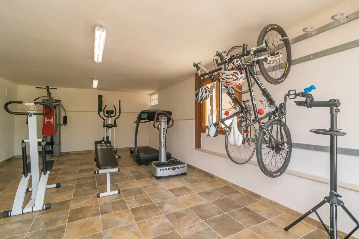 Sala de ejercicio y almacenamiento de bicicletas con máquinas y bicicletas colgadas en la pared.