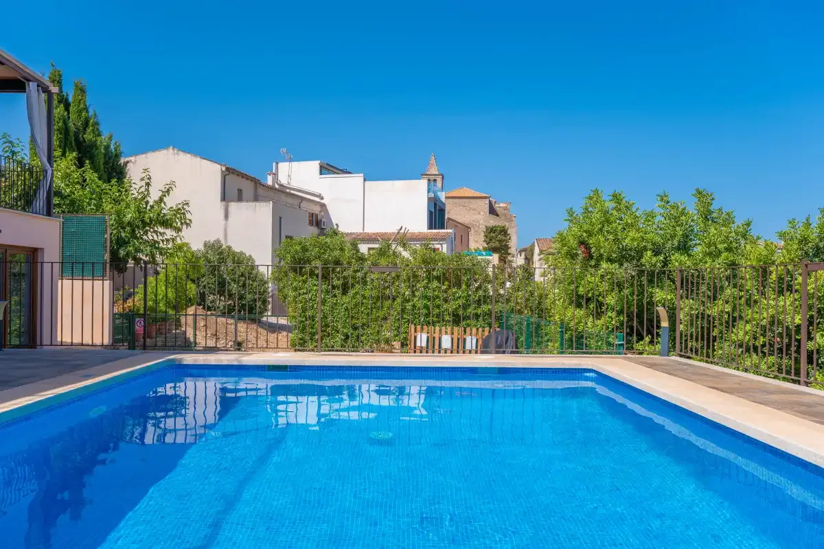 Una piscina con una zona pavimentada y vegetación al fondo.