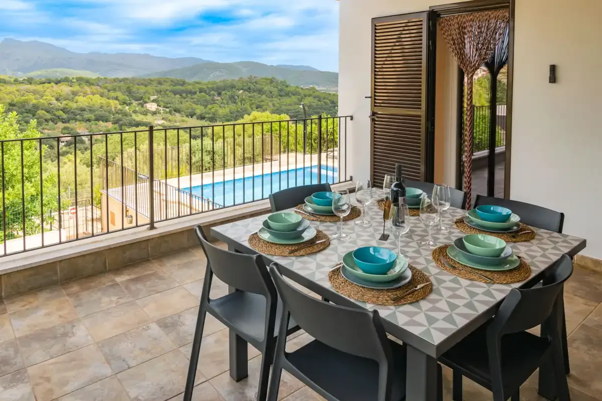 Una zona de comedor en la terraza tiene vistas a una piscina y colinas verdes.