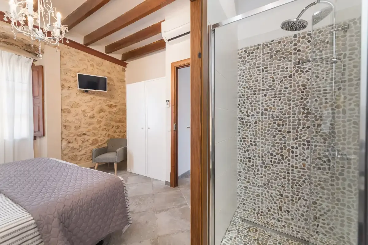 Un dormitorio con una cama y asientos junto a una ducha de cristal.