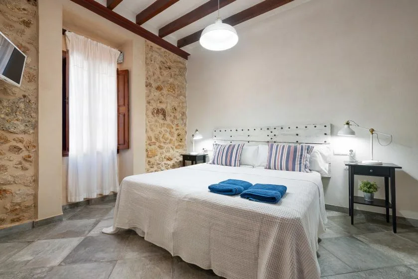 Un dormitorio con una cama bien tendida y paredes de piedra a la vista.