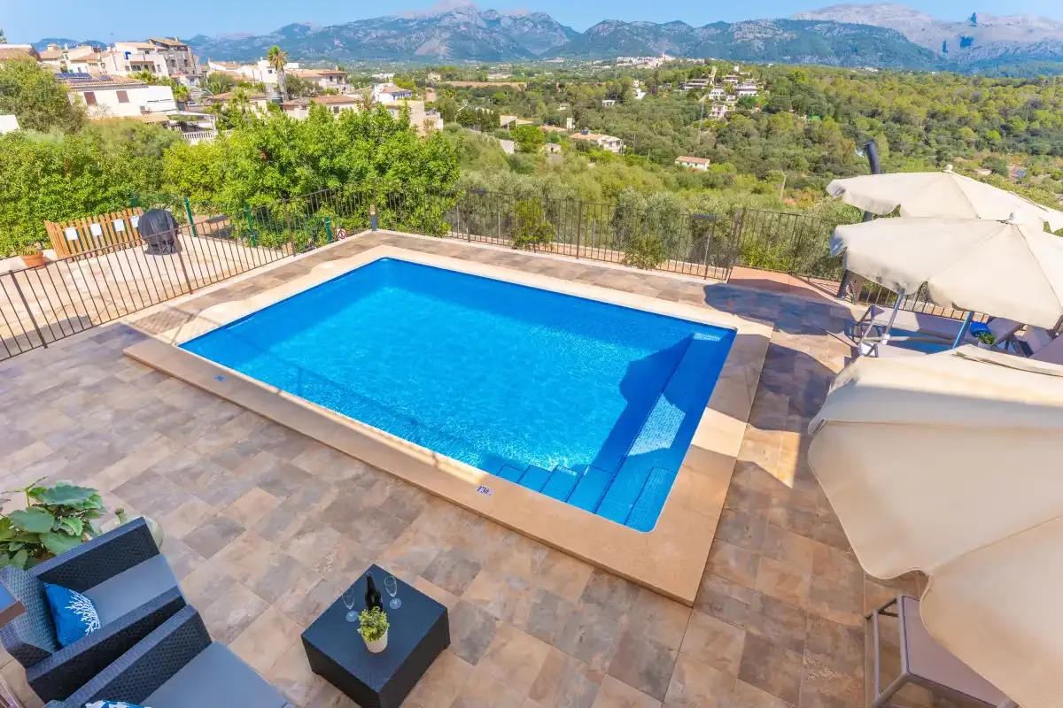 Una piscina en una terraza pavimentada ofrece vistas a una ladera verde.