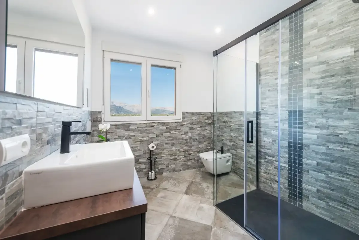 Un baño luminoso tiene un lavabo junto a una ducha de cristal.