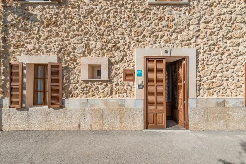 Una fachada de piedra tiene una puerta de madera abierta y ventanas con contraventanas.