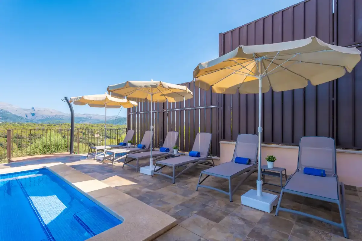 Un patio junto a la piscina con asientos reclinables y vistas abiertas a las colinas.