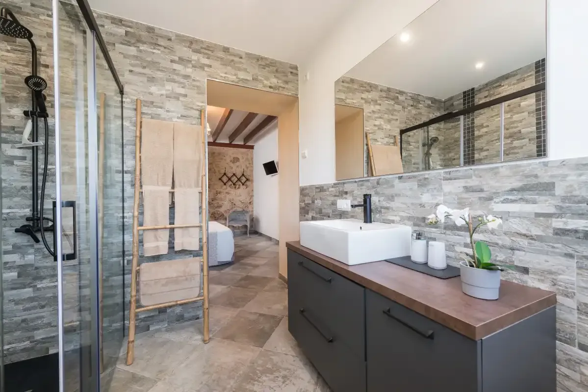 Un baño revestido de azulejos con ducha de vidrio y lavabo sobre un mueble.
