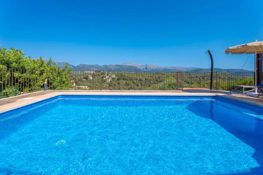 Una piscina está junto a un patio cercado, con colinas a lo lejos.
