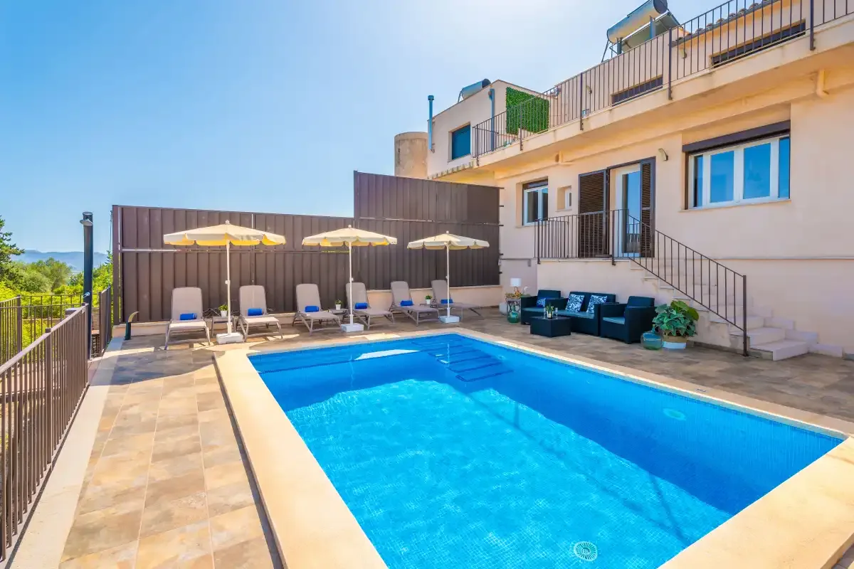 Una piscina al aire libre está junto a un edificio con asientos de descanso.