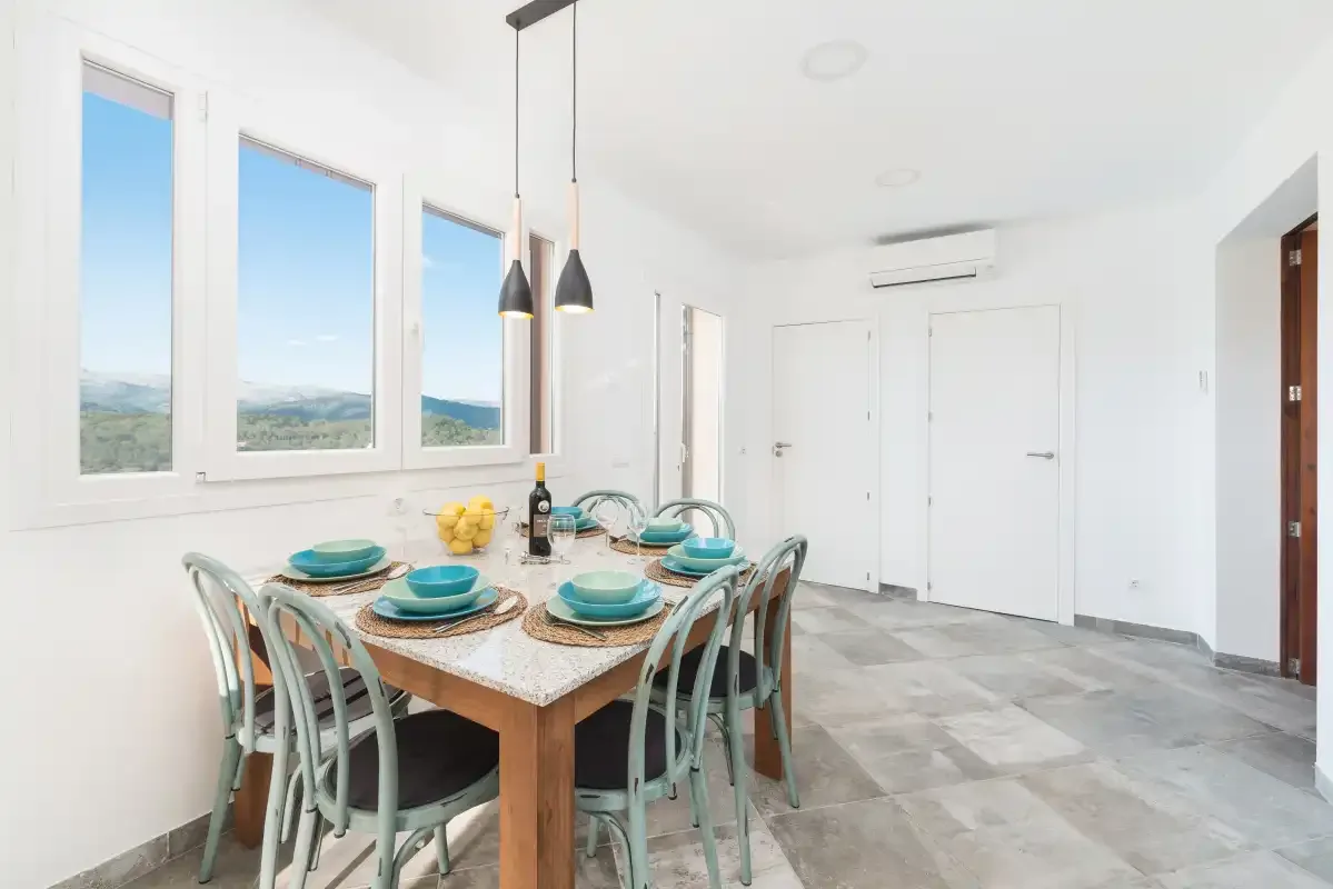 Un comedor luminoso con la mesa puesta junto a grandes ventanas.